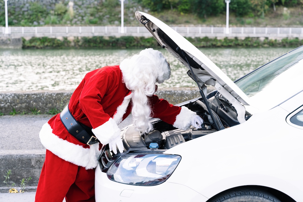 A man dresed as Santa bending over an open car bonnet checking problems & doing repairs